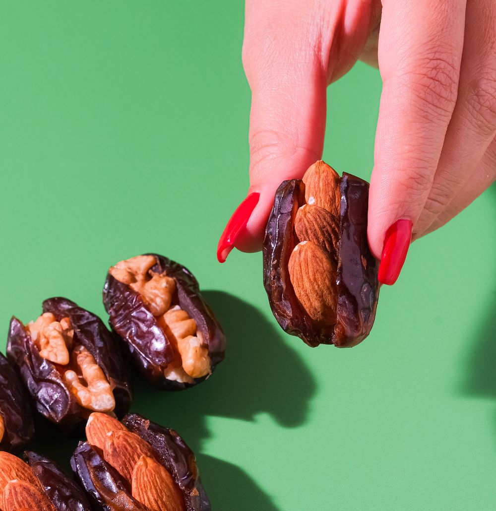 A hand picking up an almond-stuffed date, with walnut and cashew stuffed dates on a green table.