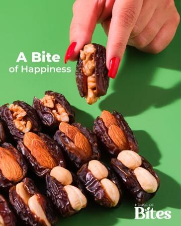 A hand picking up a walnut-stuffed date from a row of dates stuffed with almonds and cashews.